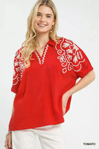 Red blouse with white floral embroidery on V neckline and decorative sleeves.