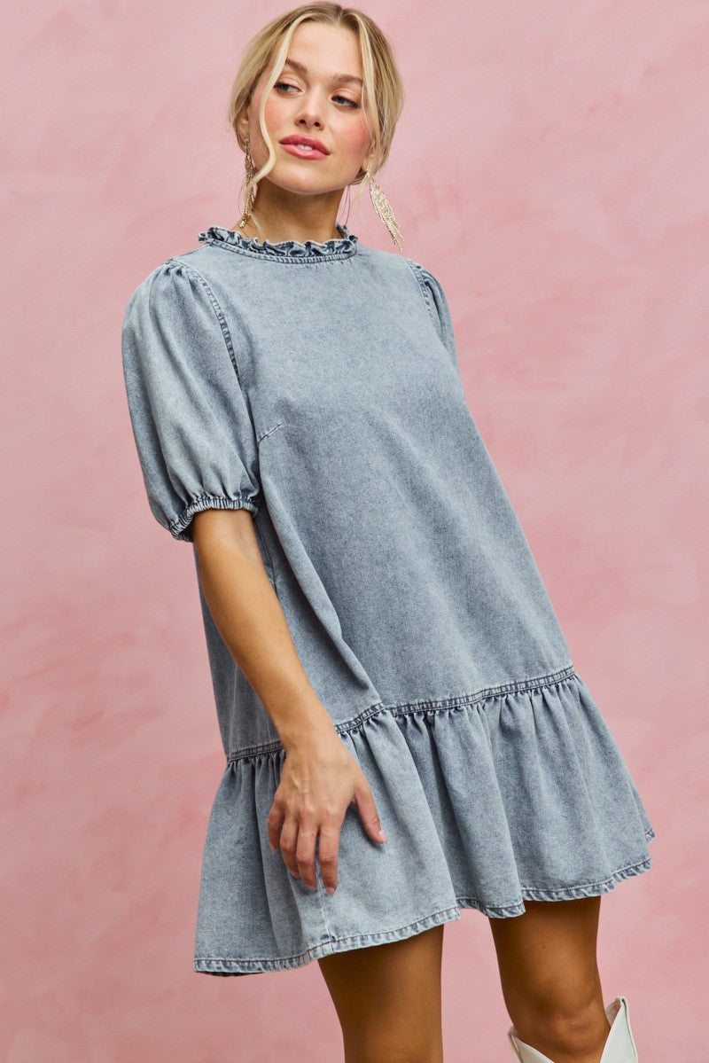 Light wash denim mini dress with ruffled neckline, puff sleeves, and gathered tiered hem