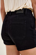 Black denim trouser shorts close-up with waistband label and back patch pocket