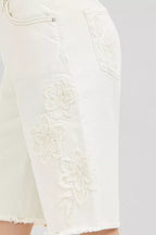 Cream denim shorts with floral embroidery applique near pocket and frayed hem