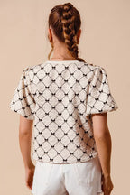 Ivory textured woven top with black bow pattern, shown from the back with puff sleeves