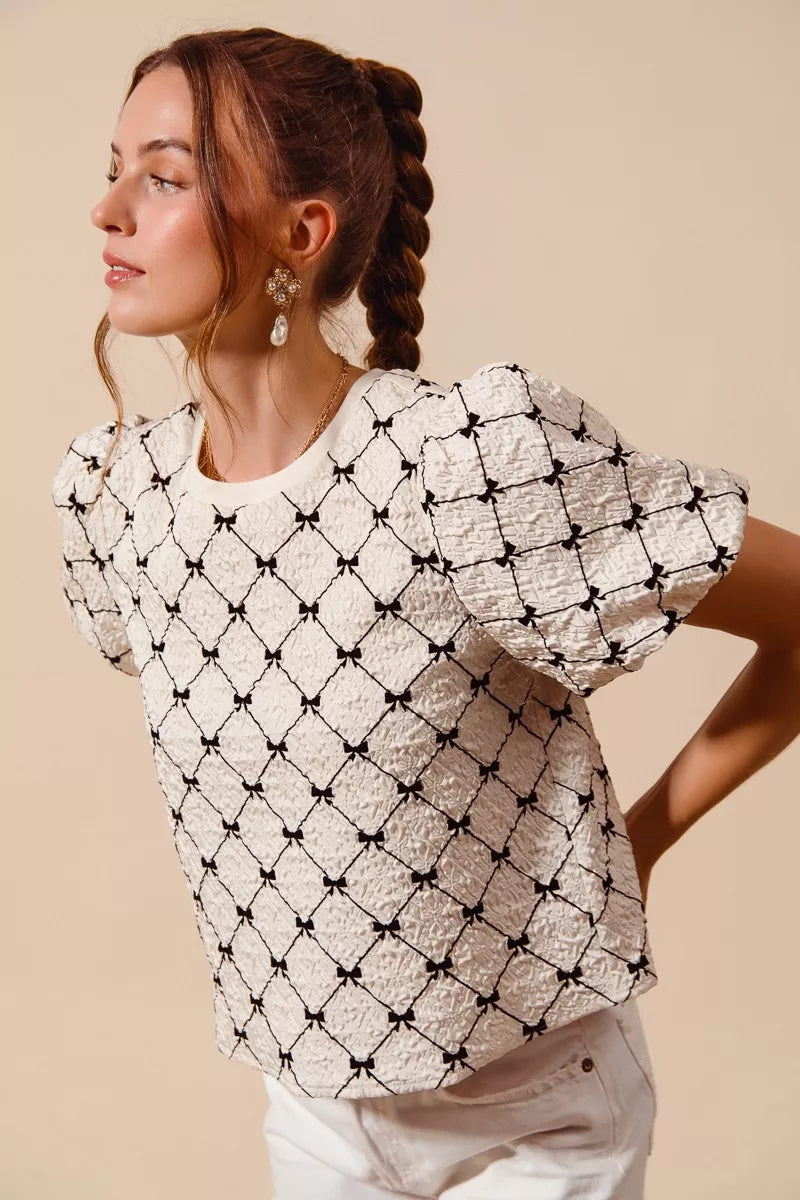Ivory textured woven top with black bow pattern and short puff bubble sleeves