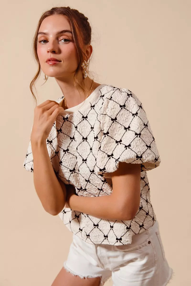 Ivory textured woven top with black bow pattern, puff bubble sleeves and crew neck