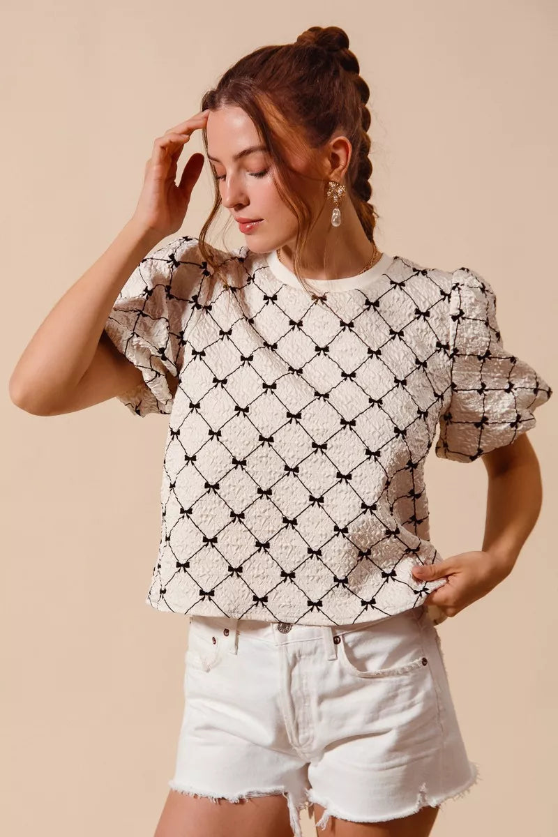Ivory textured woven top with black bow pattern and short puff bubble sleeves
