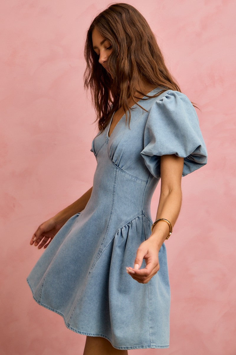 Light wash denim mini dress with V-neck and puff sleeves, back view with flared hem