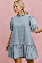 Light wash denim mini dress with ruffled neck detail and short puff sleeves, tiered skirt
