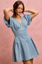 Light wash denim mini dress with V-neckline, gathered waist, and short puff sleeves