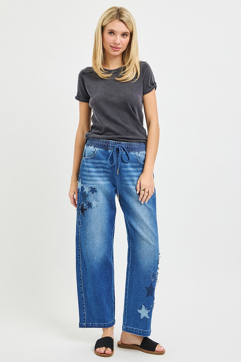 Medium-wash cropped barrel jeans with drawstring waist and star patch accents on the leg