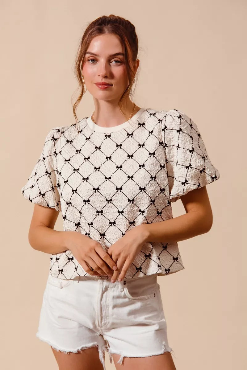 Ivory textured woven top with black bow pattern and short puff bubble sleeves