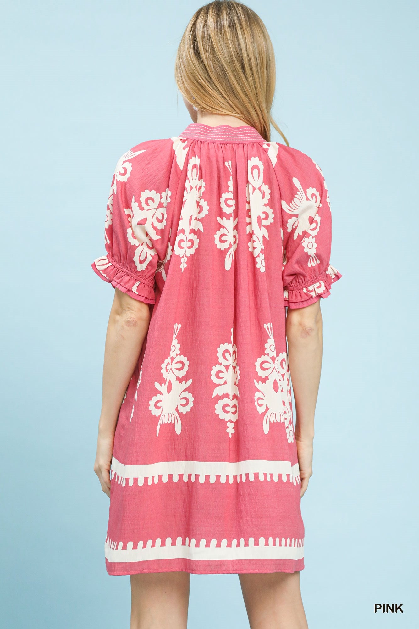Back view of pink mini dress with white floral border print and gathered yoke