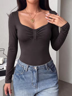 Ruched long-sleeve bodysuit with scoop neckline, dark fabric, fitted thong-style bottom