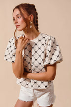 Ivory textured woven top with black bow pattern and puff bubble sleeves at side angle