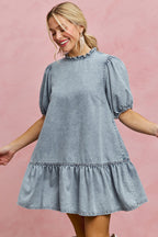 Light wash denim mini dress with ruffled high neckline, puff sleeves, and tiered skirt