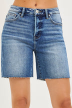 Medium-wash denim shorts close-up: button fly, belt loops, raw frayed hem.