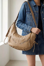 Beige crescent shoulder bag on a model with adjustable strap and front zip pocket
