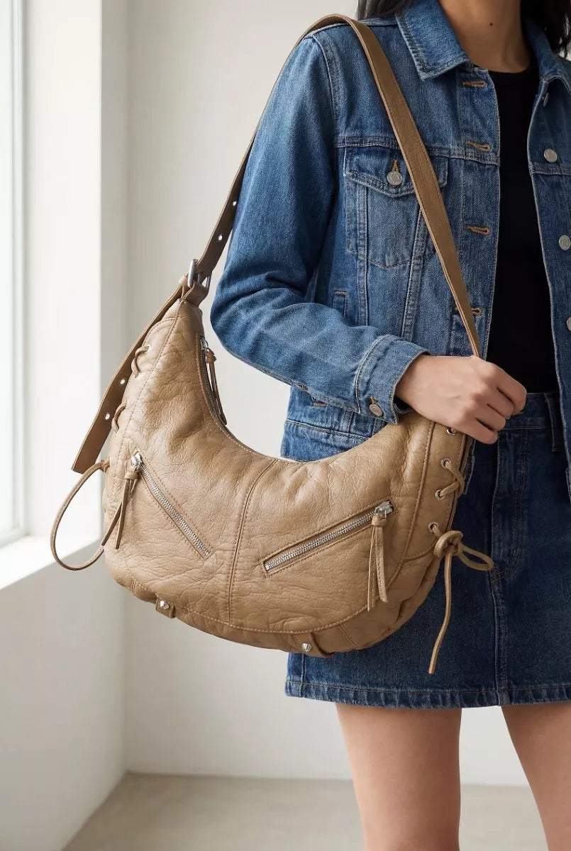 Beige crescent shoulder bag on a model with adjustable strap and front zip pocket
