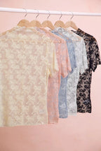 Assorted sheer mesh tops with bow-like lace pattern on hangers, short sleeves