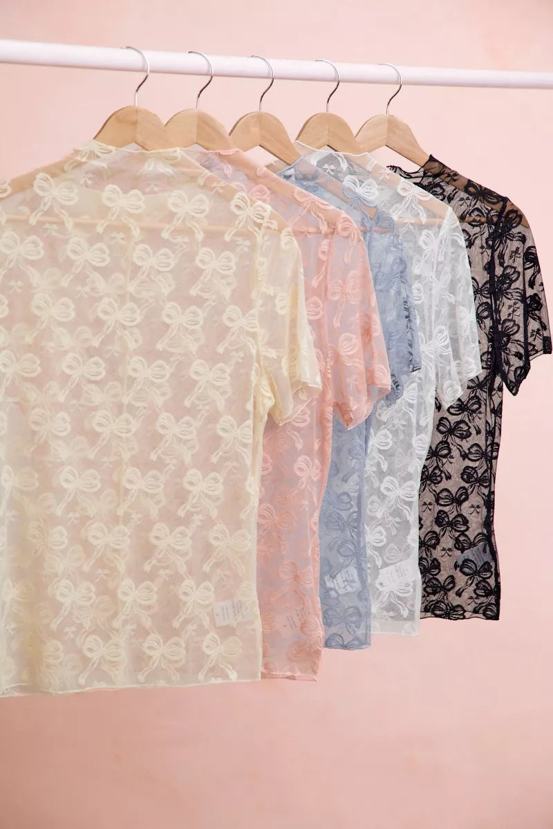Assorted sheer mesh tops with bow-like lace pattern on hangers, short sleeves