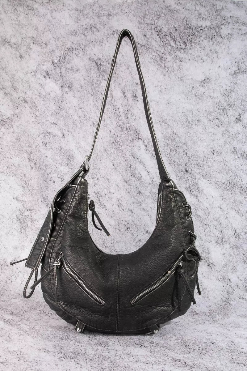 Black crescent shoulder bag with double straps, zip pocket, and braided tassel details