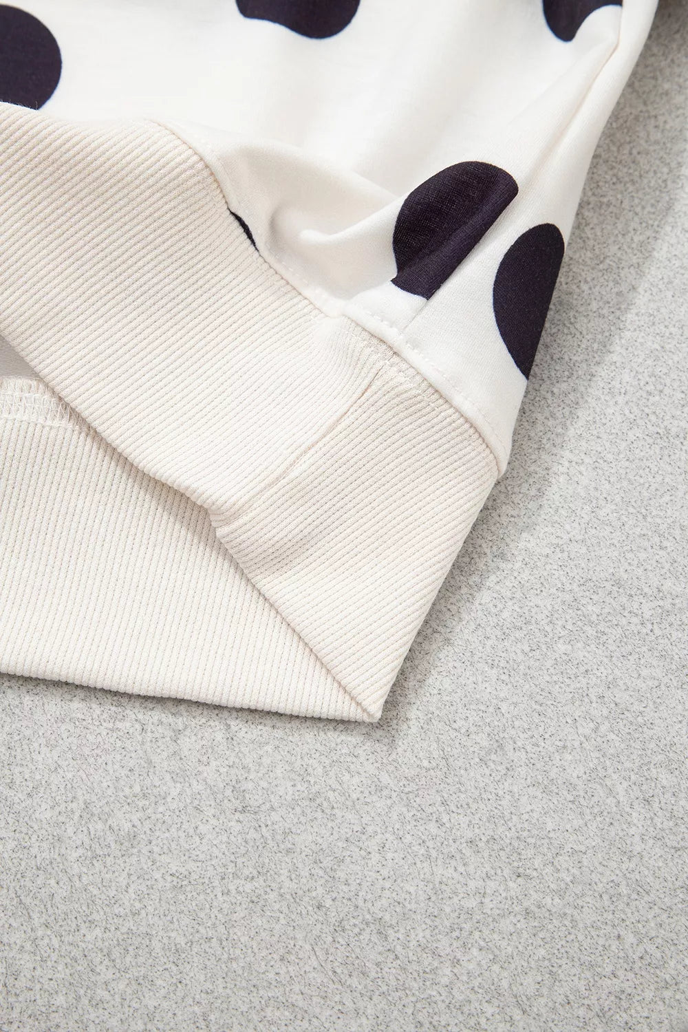 Close-up of sweatshirt hem and sleeve cuff; white knit with black polka dots