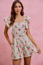 Ivory floral print denim romper with ruffled cap sleeves and belted, pleated skirt