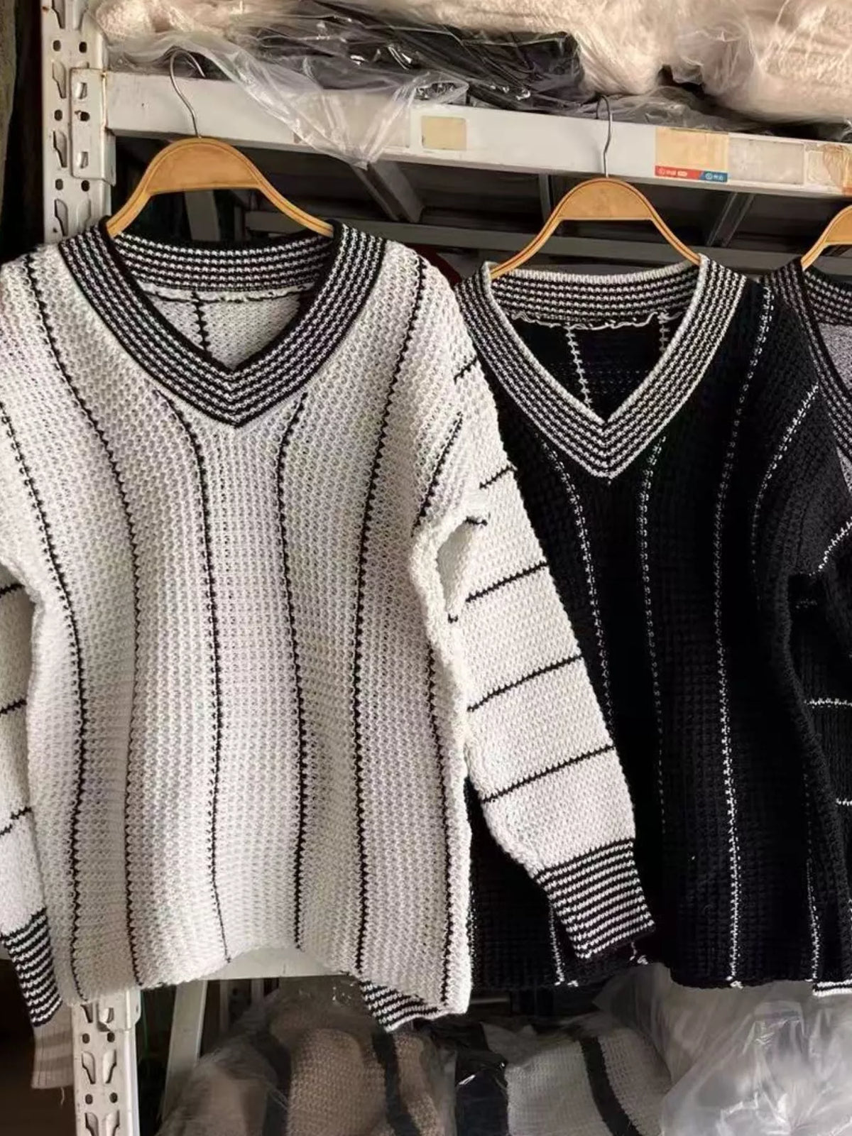 Textured knit V-neck sweaters on hangers: light cream and black with contrast trim.