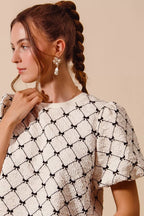 Ivory textured woven top with black bow pattern and short puff bubble sleeves, close up