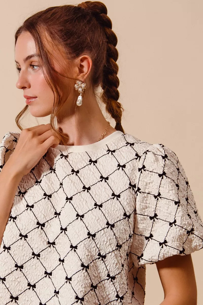 Ivory textured woven top with black bow pattern and short puff bubble sleeves, close up