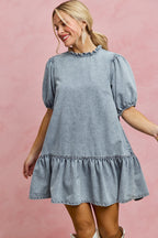 Light-wash denim mini dress with ruffled neckline and puff sleeves, tiered hem