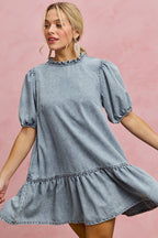 Light wash denim mini dress with ruffled high neckline and puff sleeves, tiered skirt