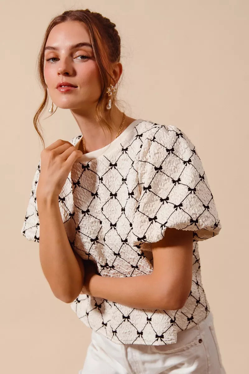 Ivory textured woven top with black bow pattern and puff bubble sleeves