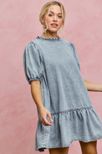 Light wash denim mini dress with ruffled high neckline and puff sleeves, tiered skirt