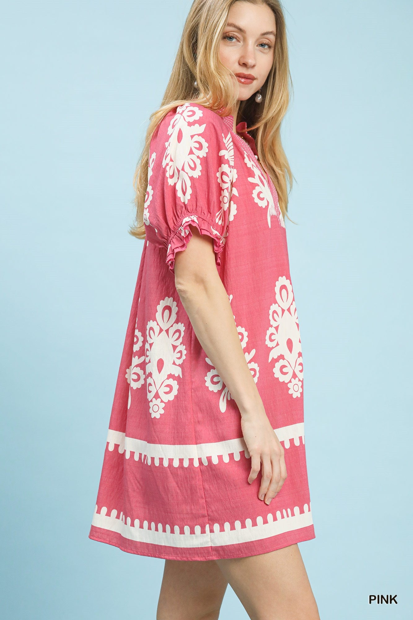Pink mini dress with white floral border print, puff sleeves, and ruffle trim