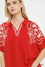 Red blouse close-up with white floral embroidery on the V neckline and sleeve.