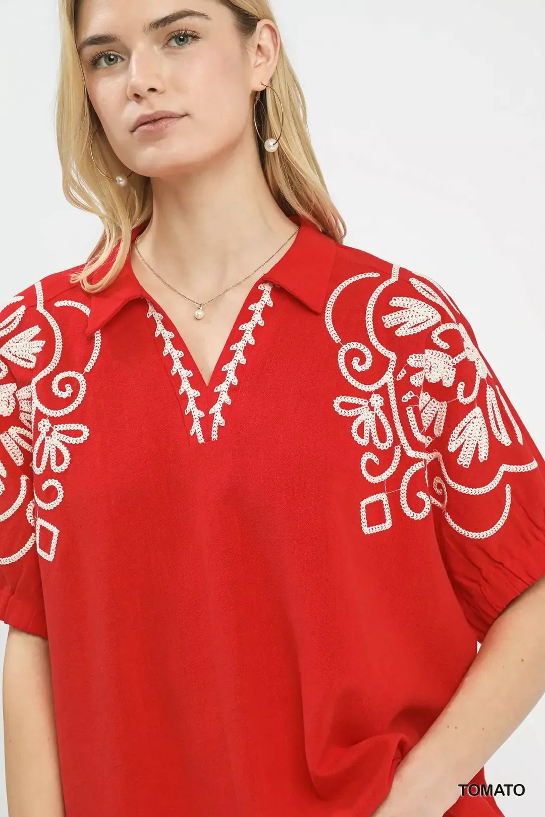 Red blouse close-up with white floral embroidery on the V neckline and sleeve.
