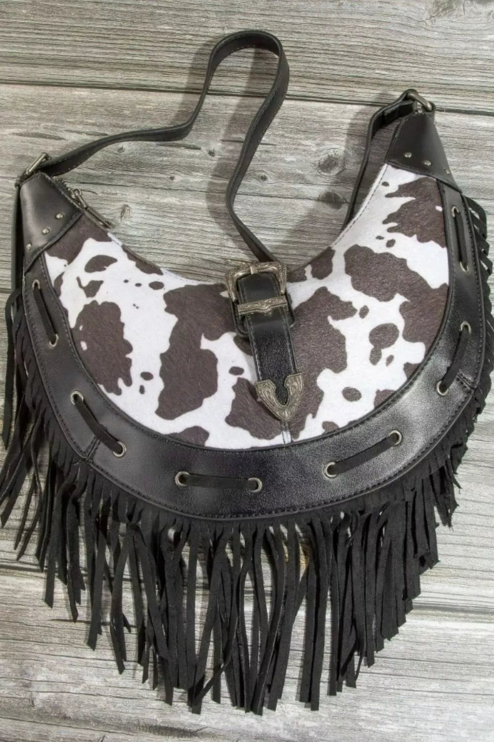 Cow print faux leather fringe hobo bag with metal buckle front and dangling tassels