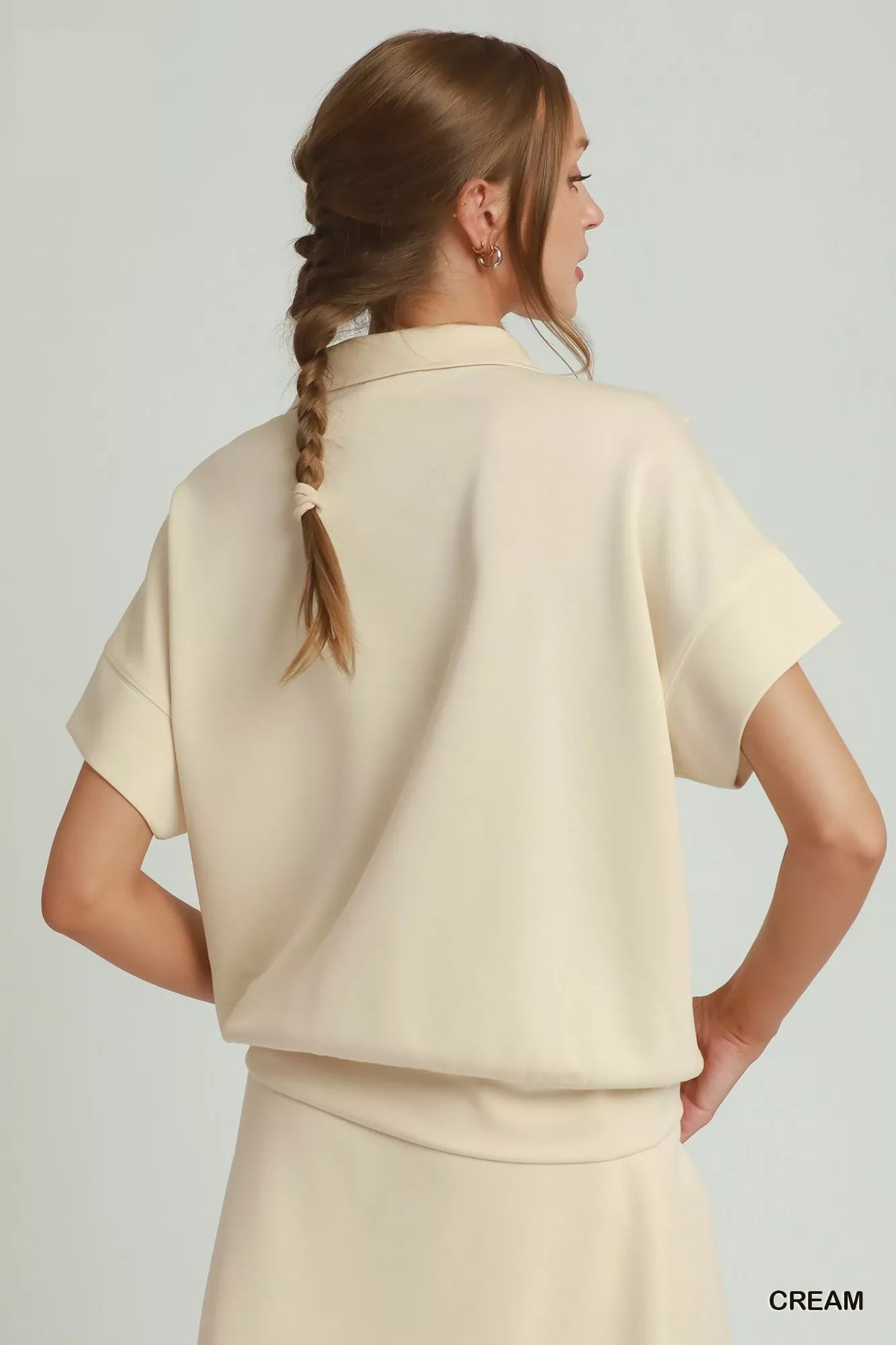 Cream quarter-zip short-sleeve top with ruffle-trim collar, shown from the back