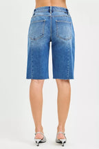 Back view of medium-wash raw-hem denim jorts with button fly and patch pockets