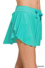 Turquoise athletic skort side view with elastic waist and tied drawstring, ruffle hem