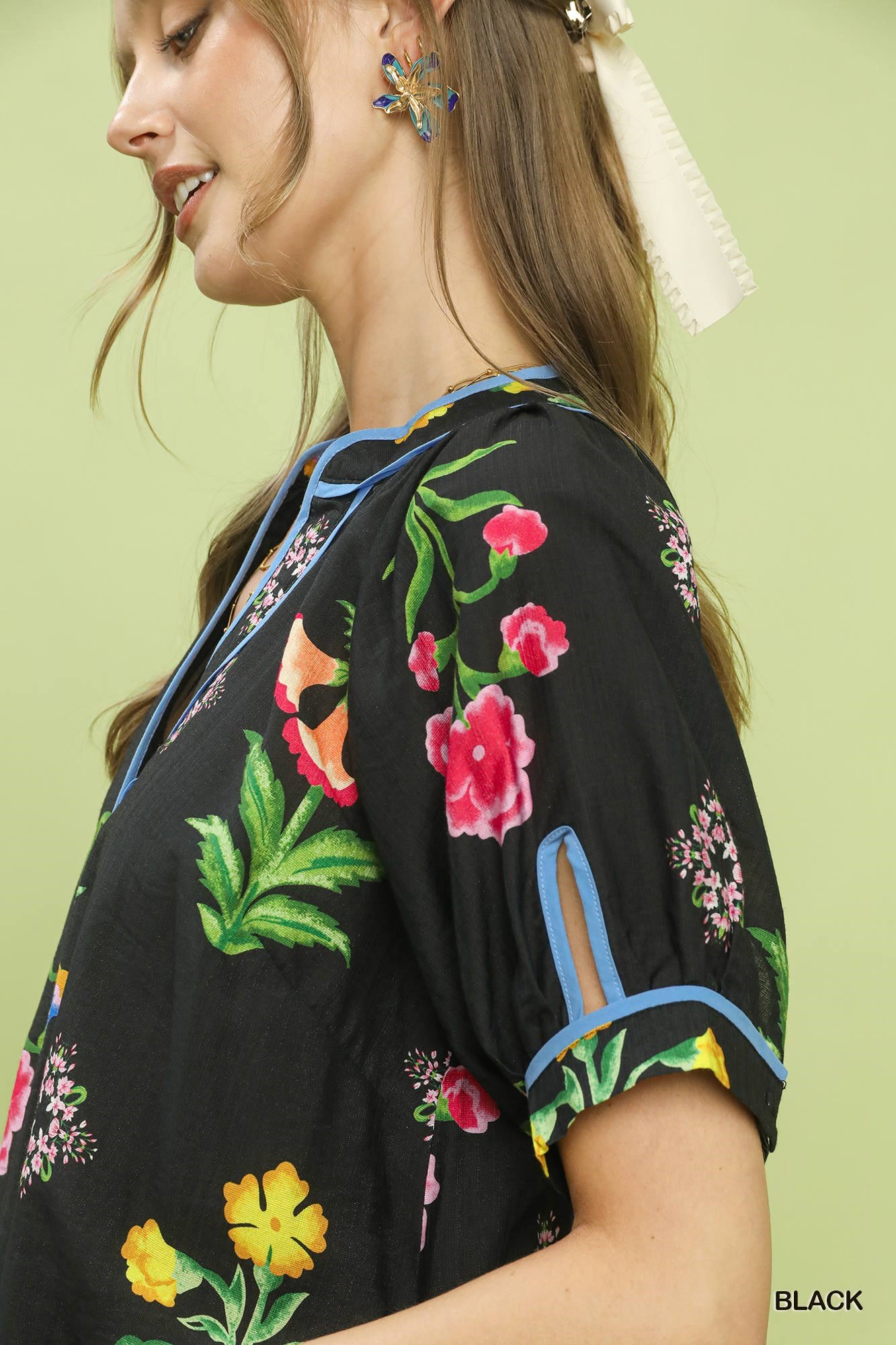 Black botanical print blouse with blue trim and short cuff sleeves, side view