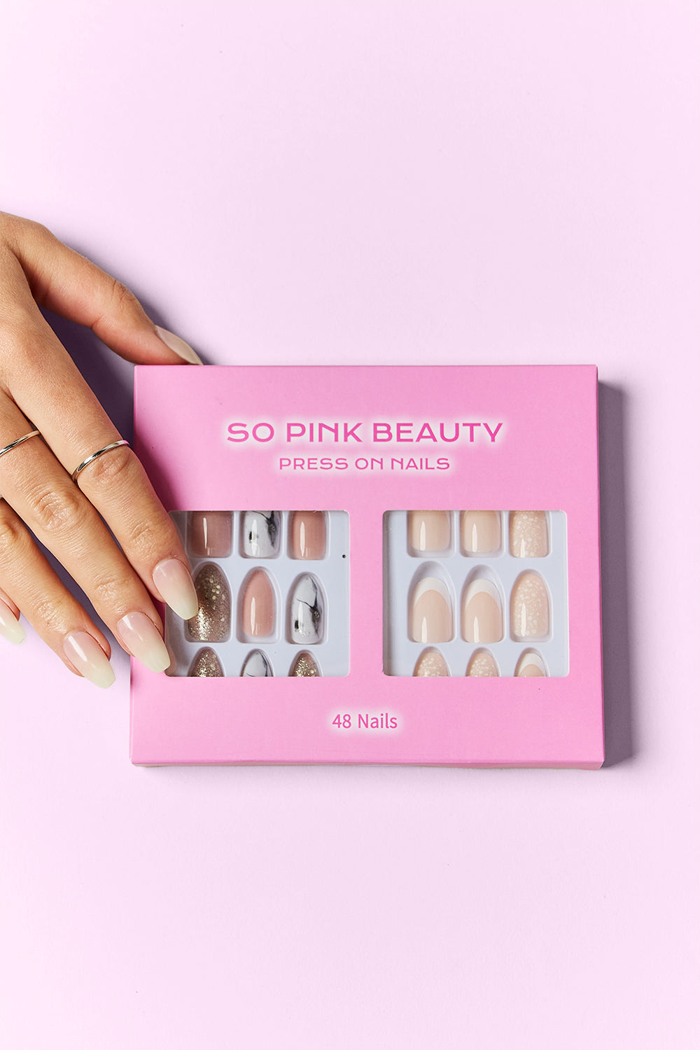 Press-on nails box in hand, showing nude, gray, and glitter oval nail designs